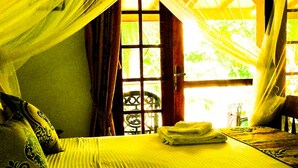 A bed with a neatly folded towel, a window with a view of greenery, and a chair in the corner. - Mahi Villa (Bentota)