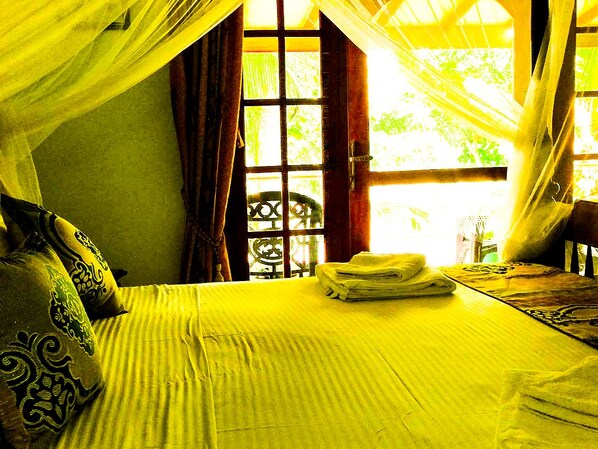 A bed with a neatly folded towel, a window with a view of greenery, and a chair in the corner. - Mahi Villa (Bentota)