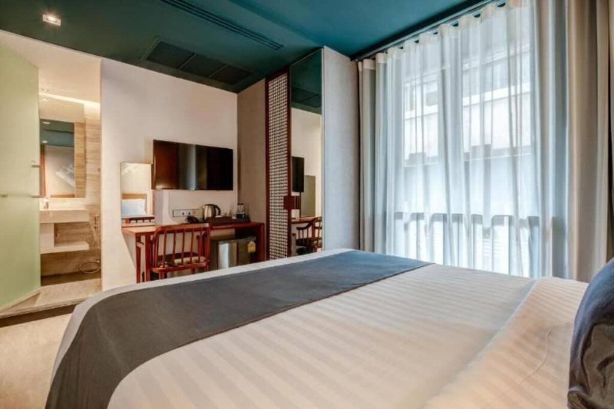 A hotel room with a bed, a desk, a chair, a television, and a large window with curtains.