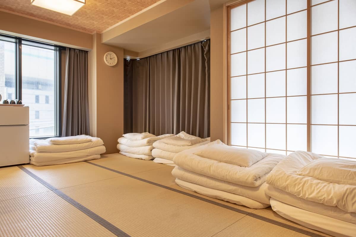 A room with tatami flooring, a large shoji screen, and neatly stacked white towels.