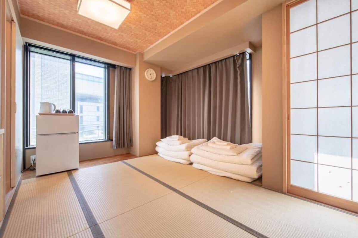 A traditional Japanese room with tatami flooring, a shoji screen, and a stack of white towels.