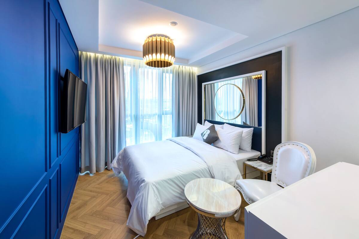 A modern hotel room with a large bed, a bedside table, a chair, and a TV mounted on the wall.