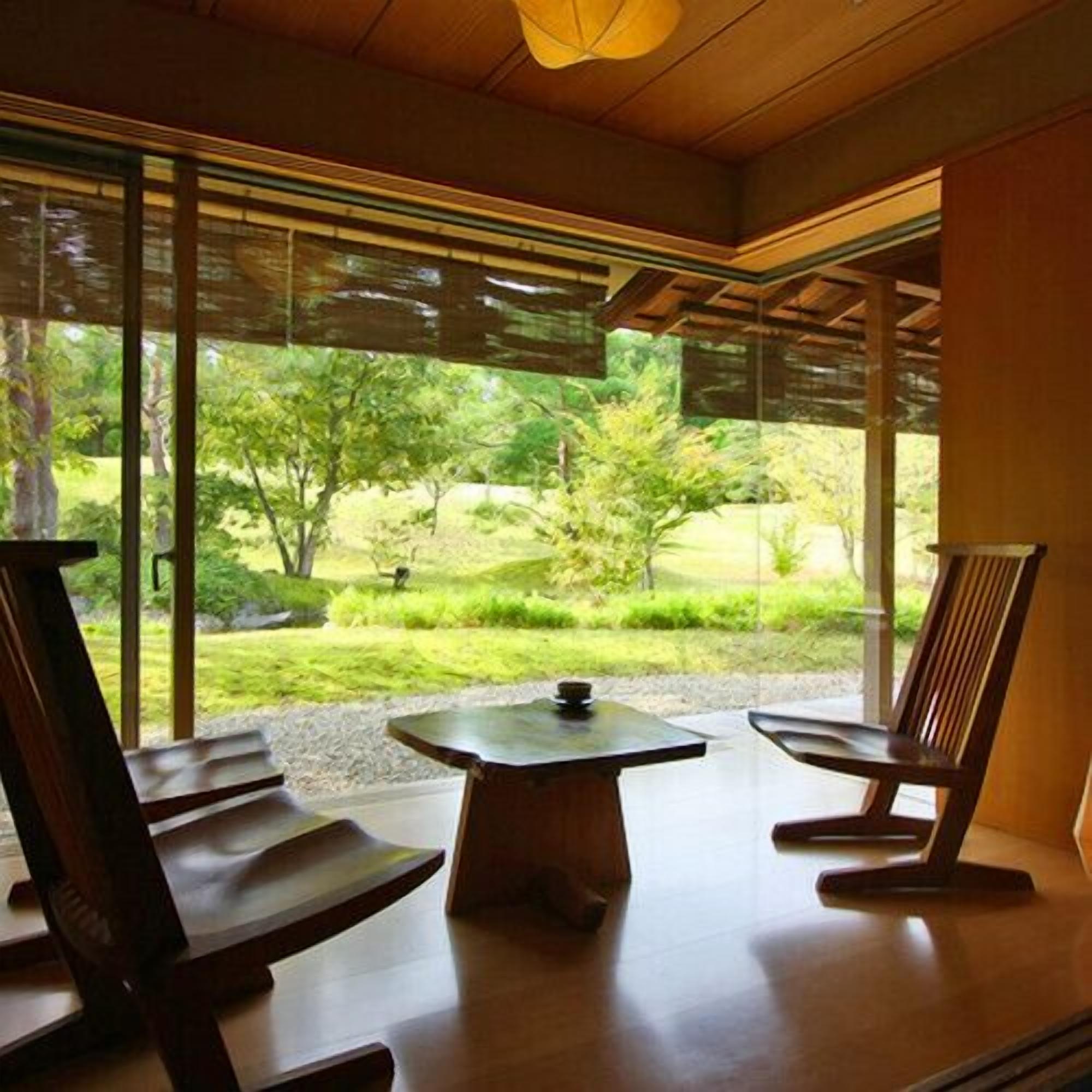 A room with a large window, a wooden table, and two wooden chairs.
