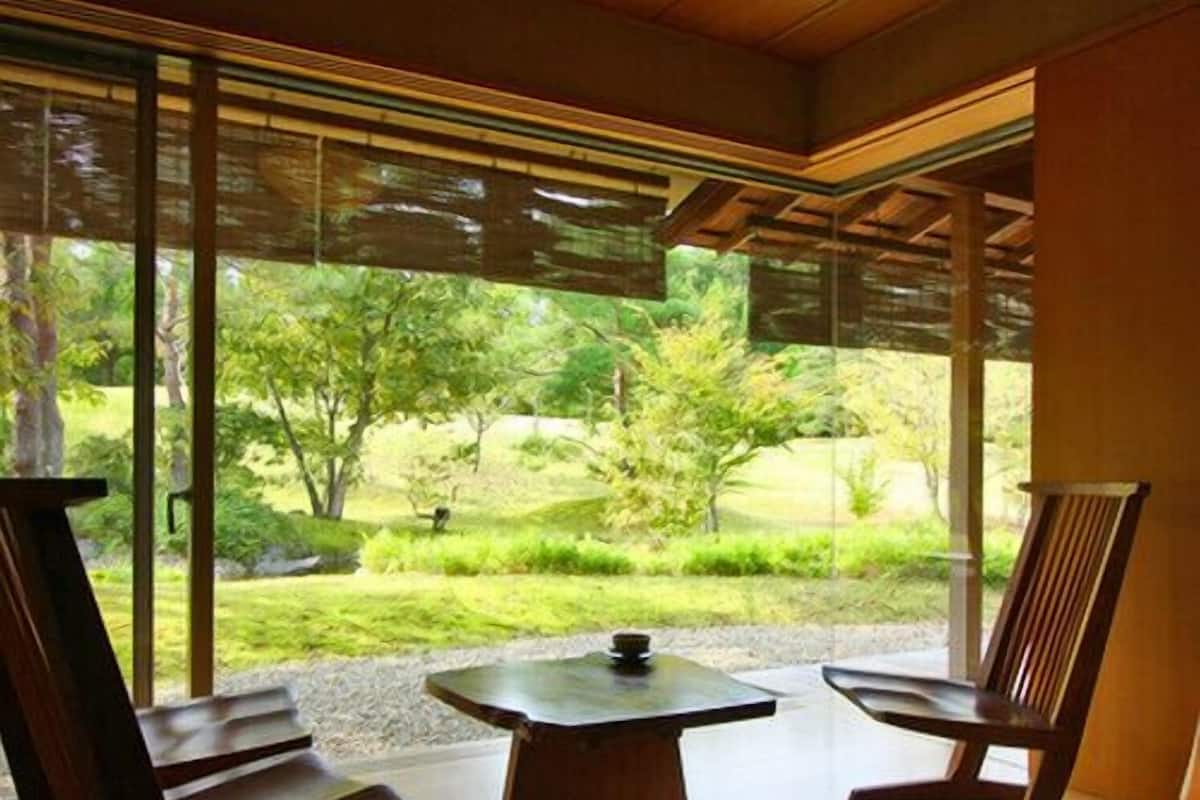 Una habitación con un ventanal grande, una mesa de madera y dos sillas de madera.
