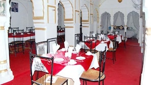 Un comedor con mesas dispuestas para el servicio, con alfombra roja y manteles blancos.