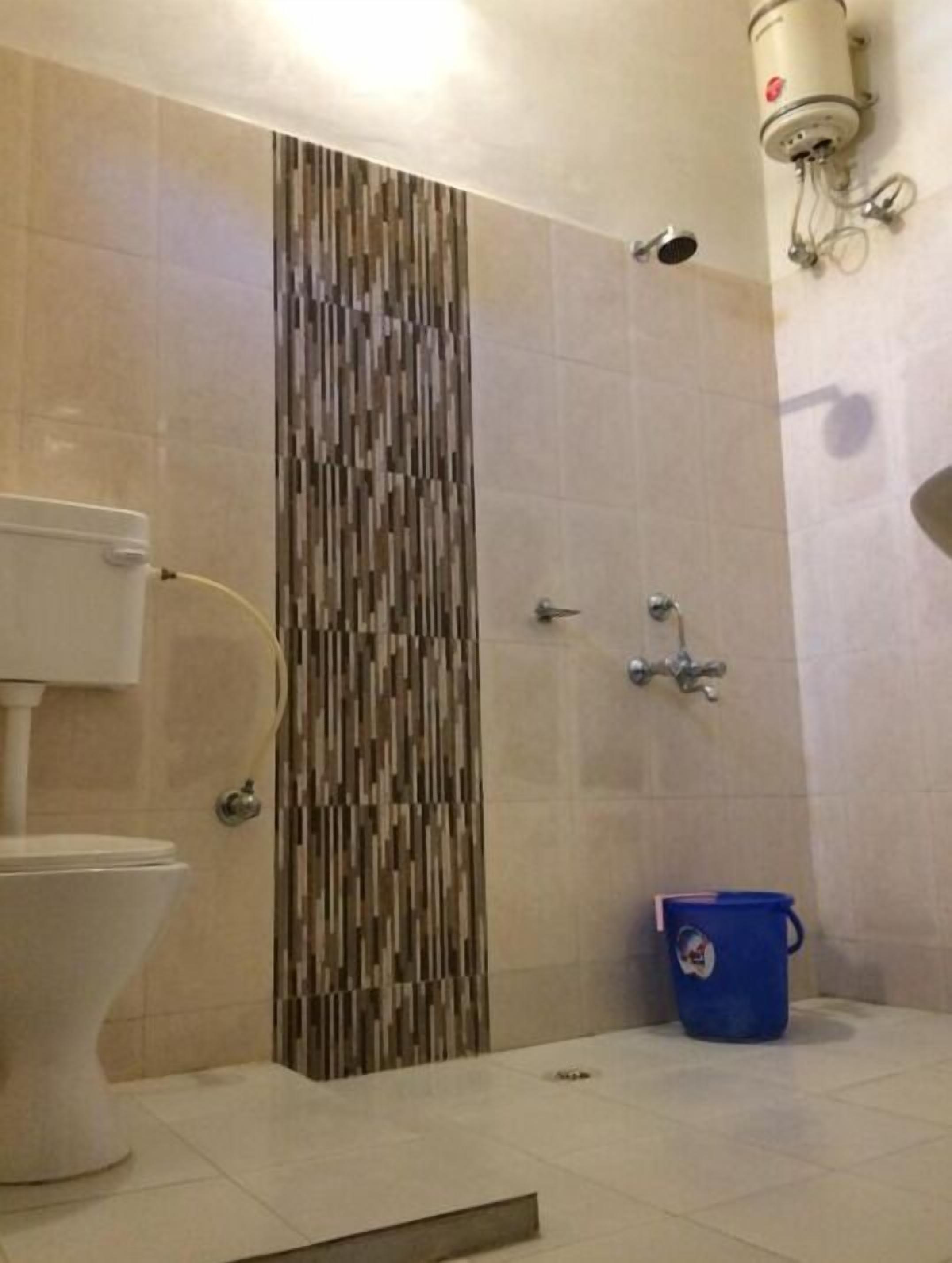 A bathroom with a toilet, a shower, and a blue bucket.