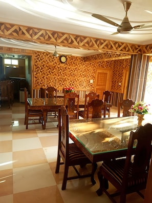 A dining area with a glass-top table, wooden chairs, and a ceiling fan. - Grand Noora Palace (Srinagar)