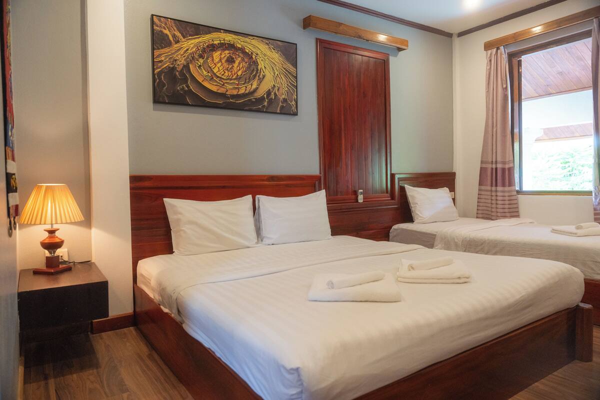 Een hotelkamer met twee bedden, een houten hoofdeinde, een schilderij aan de muur en een raam met gordijnen.