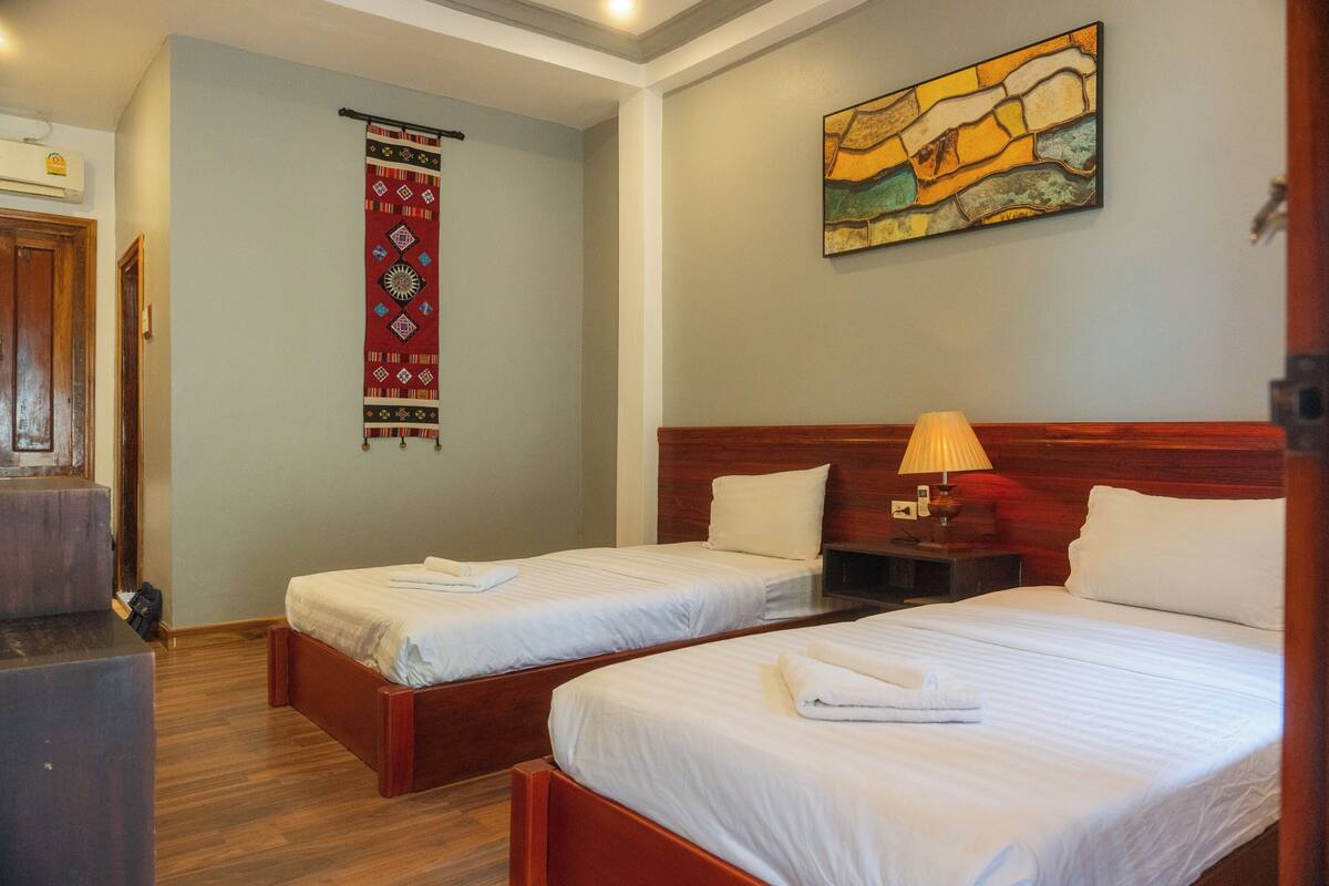 Een hotelkamer met twee bedden, een houten hoofdbord, een wandlamp en een decoratief wandtapijt.