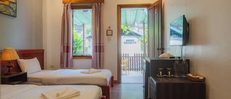 Habitación de hotel con dos camas, televisión, escritorio con lámpara y vista al exterior.