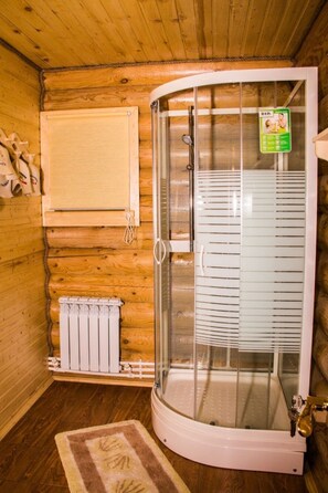 A wooden cabin with a glass-enclosed shower, a radiator, and a wooden wall with a towel rack. - Nikitskoe podvorie (Maurino)