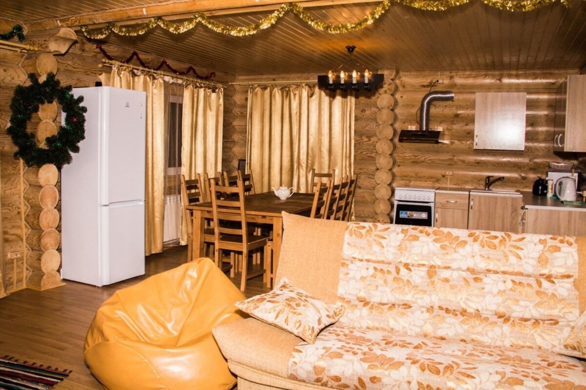 A cozy log cabin interior with a dining area, kitchenette, and a sofa with a patterned throw.