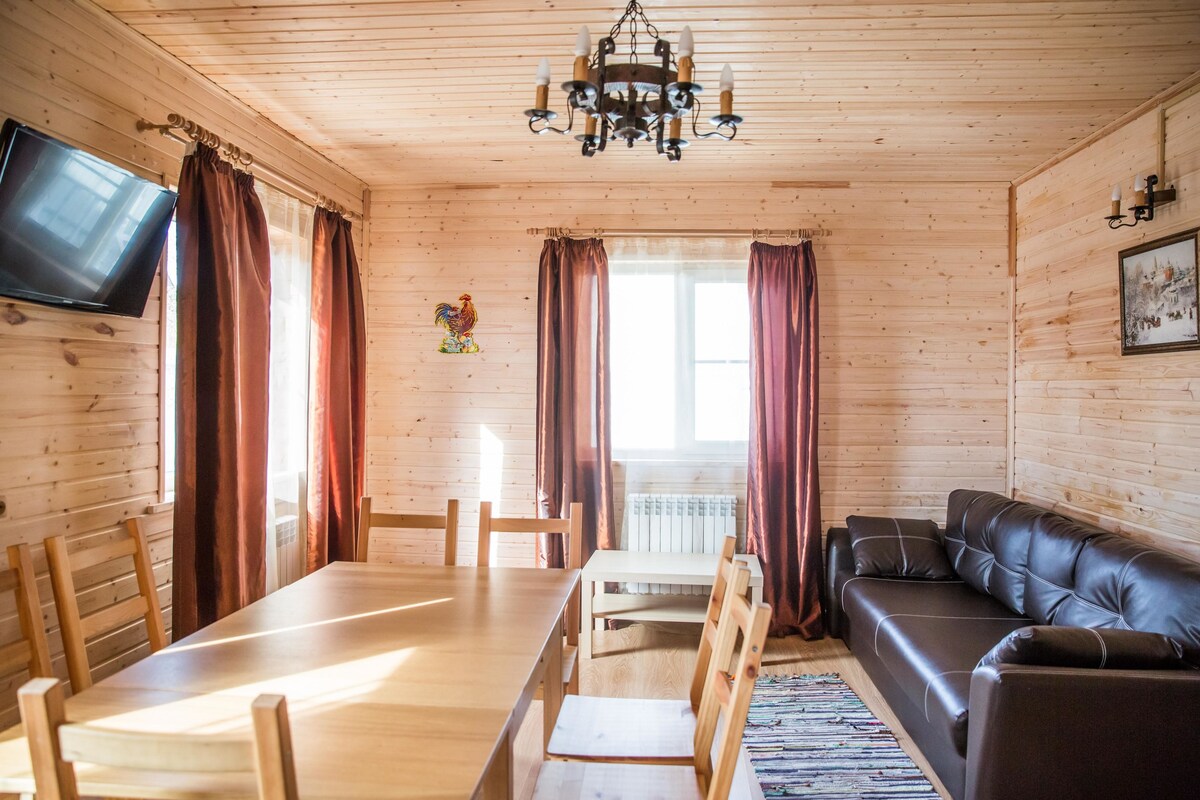 A wooden-paneled room with a dining table, chairs, a sofa, a TV, and a chandelier.