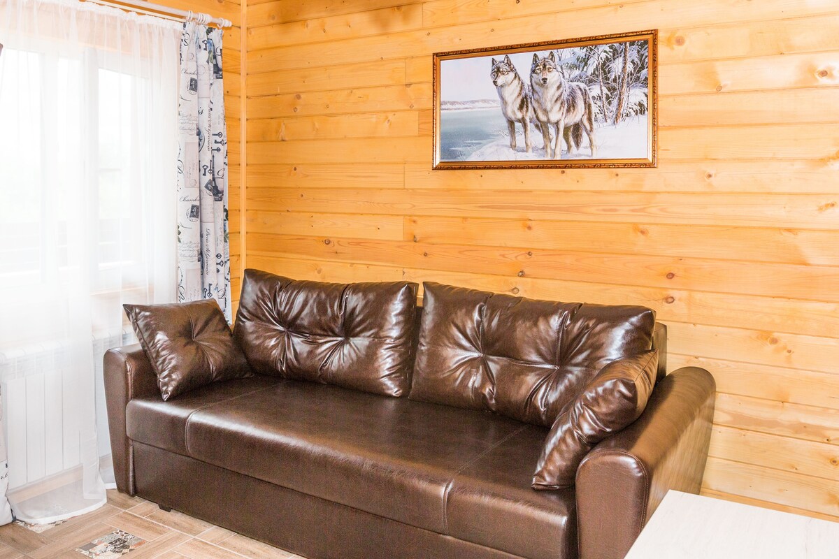 A brown leather sofa against a wooden wall with a framed picture of wolves.