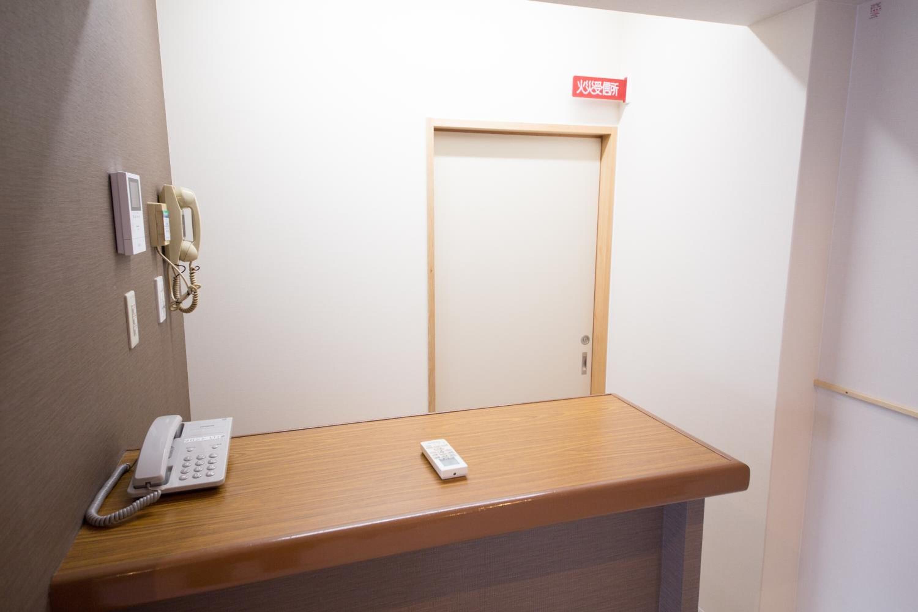 A reception desk with a telephone, a remote control, and a sign above a door.