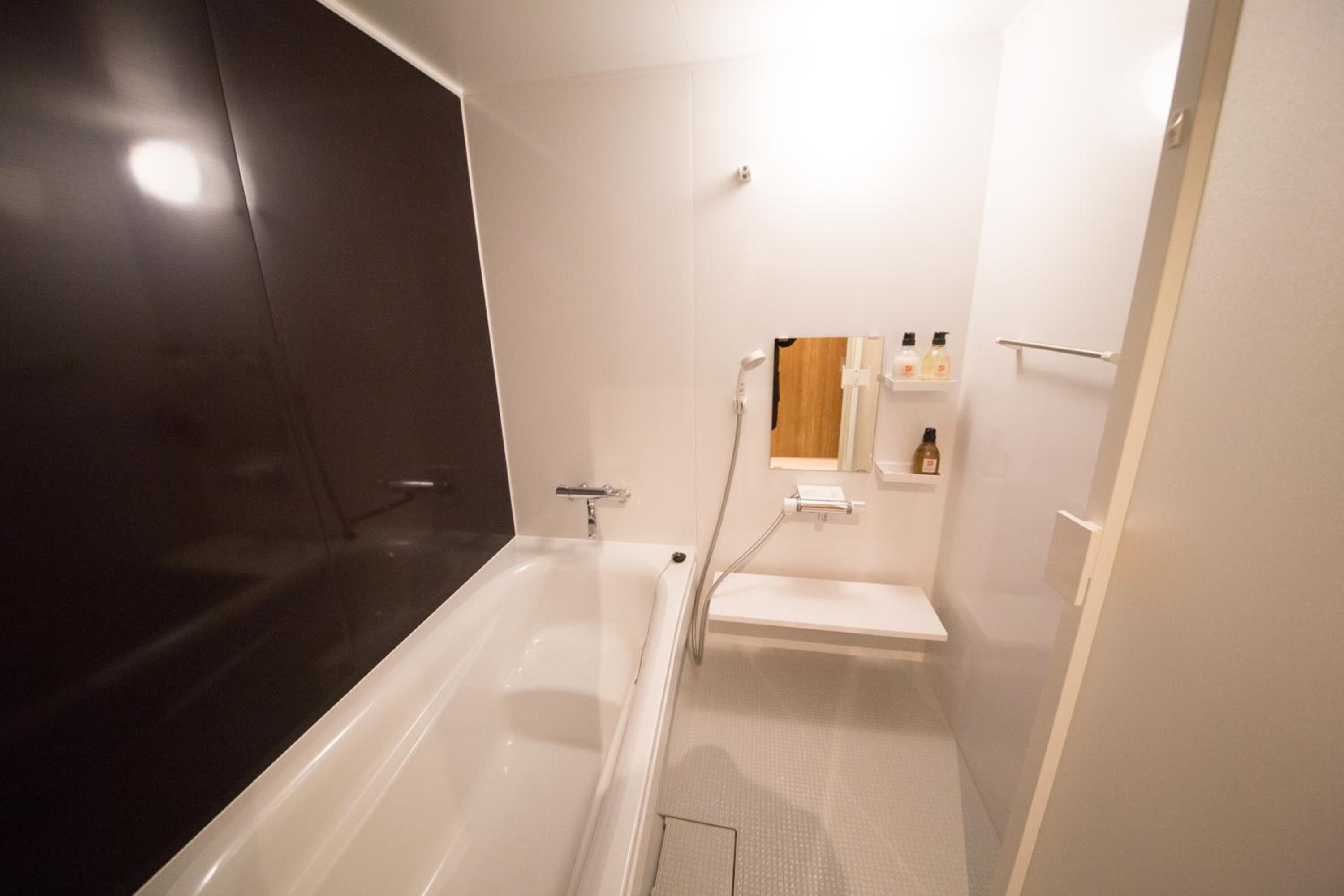 Une salle de bain moderne équipée d’une baignoire, d’une douche et d’un petit meuble-lavabo avec un miroir et des étagères.