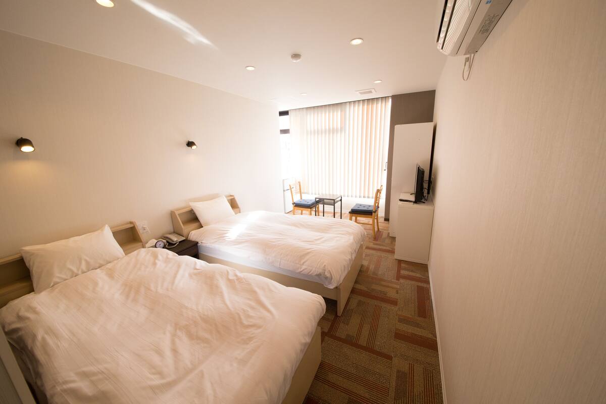 A hotel room with two beds, a small table, chairs, and a TV.