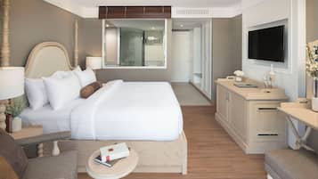 Ein Hotelzimmer mit einem großen Bett, Nachttischen, einem Schreibtisch, einem Fernseher und einem durchgehenden Türspalt sichtbaren Badezimmer.
