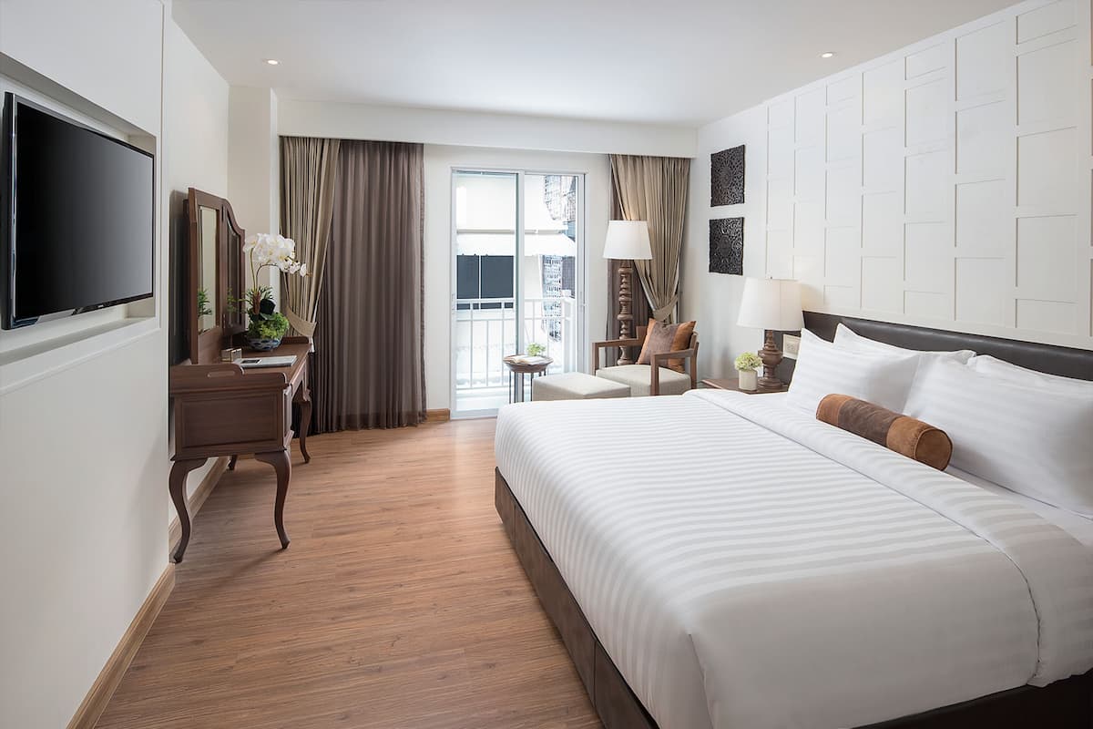 A hotel room with a large bed, a desk with a TV, a chair, a lamp, and a view of the outdoors.