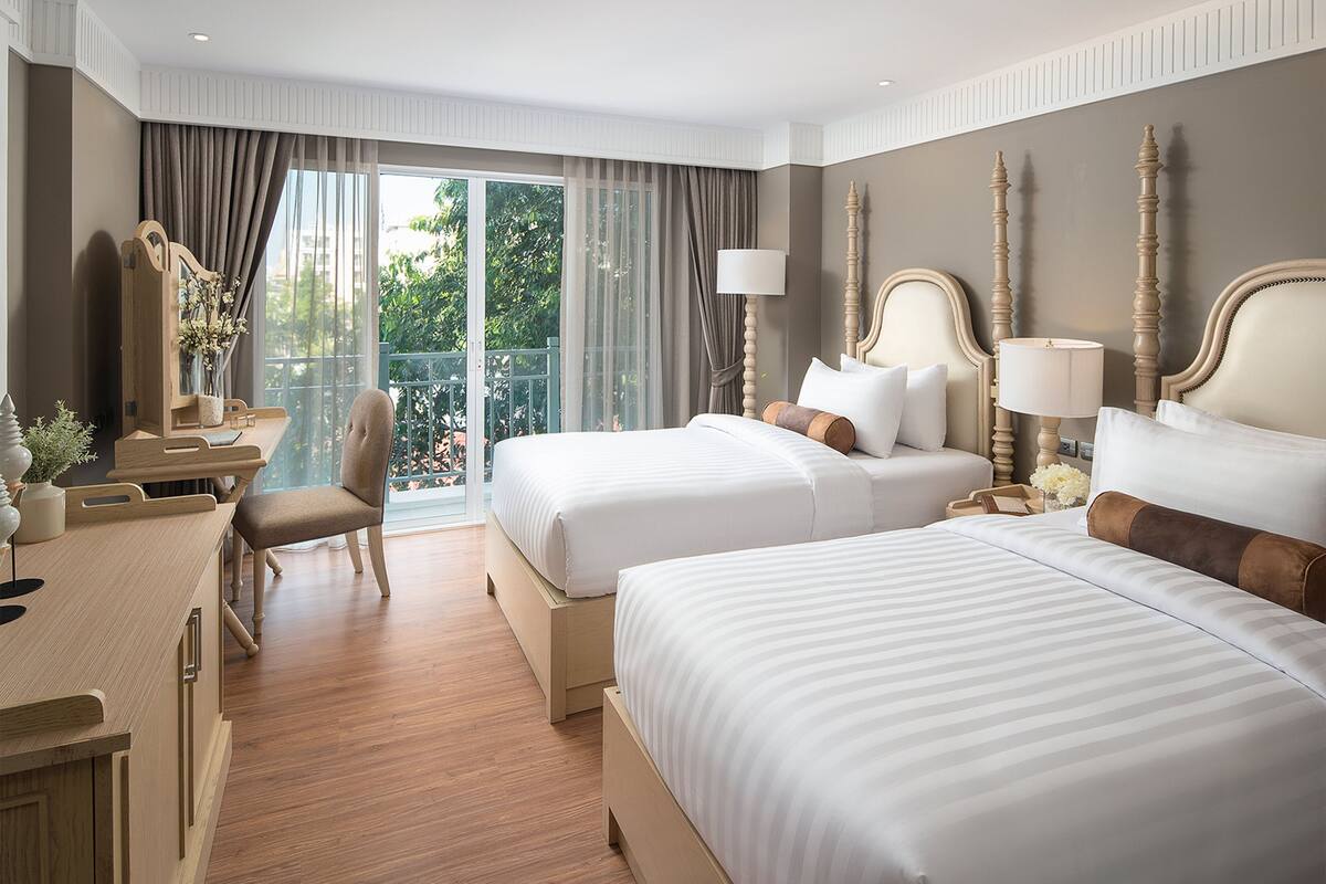 A hotel room with two beds, a desk, and a chair.
