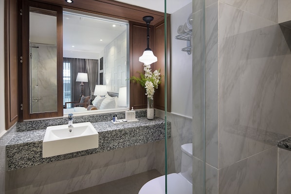 A modern bathroom with a granite countertop, a white sink, a large mirror, and a shower area. - Casa Vimaya Riverside (Bangkok)