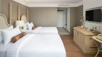 A hotel room with two beds, a wooden dresser, a television, and a door leading to another room.
