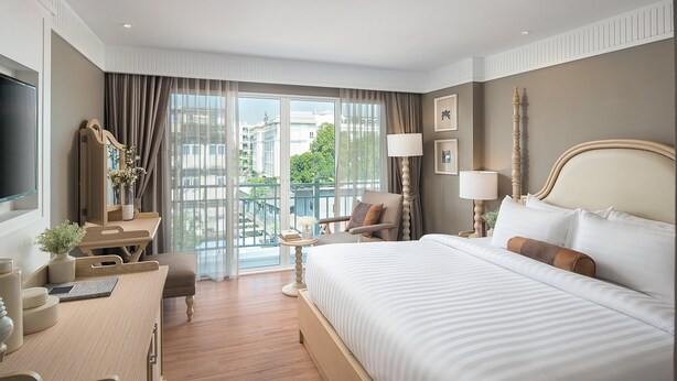 Ein Hotelzimmer mit einem großen Bett, einem Schreibtisch, einem Sessel, einem Fernseher und Blick auf die Stadt durch das Fenster.