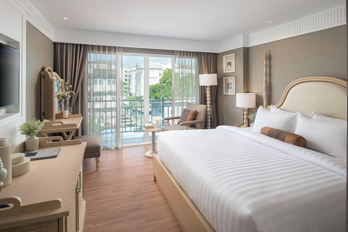A hotel room with a large bed, a desk, a chair, a TV, and a view of the city through the window.