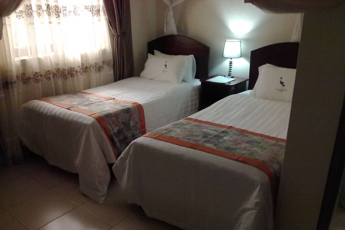 A hotel room with two single beds, a nightstand with a lamp, and a window with curtains.