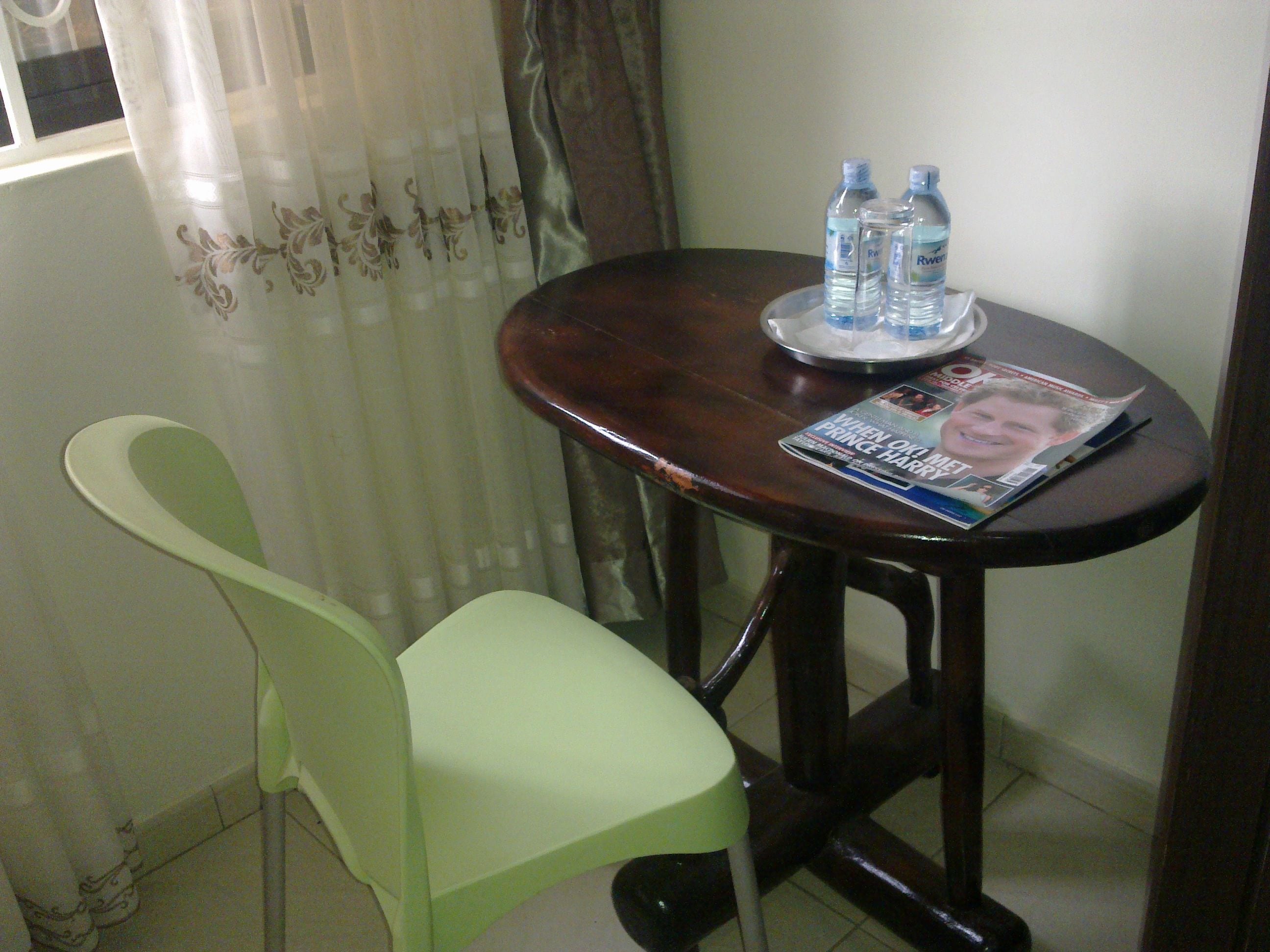 A small dining area with a table, two water bottles, a magazine, and a green chair.