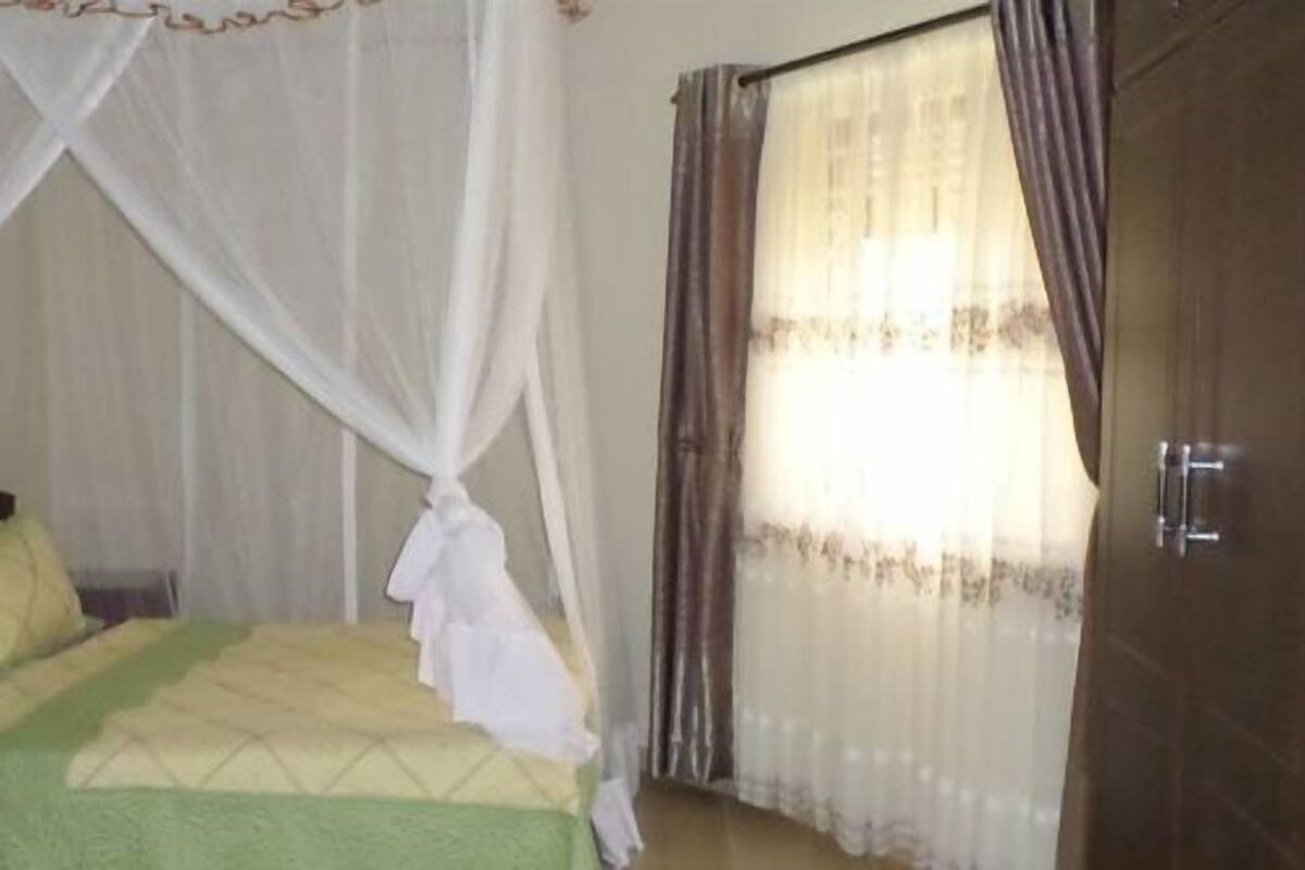 A bedroom with a bed, a nightstand, a wardrobe, and a window with curtains.