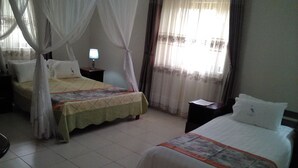 A hotel room with two beds, a nightstand with a lamp, and a window with curtains. - The Crested Crane Bwindi (Kyesero)