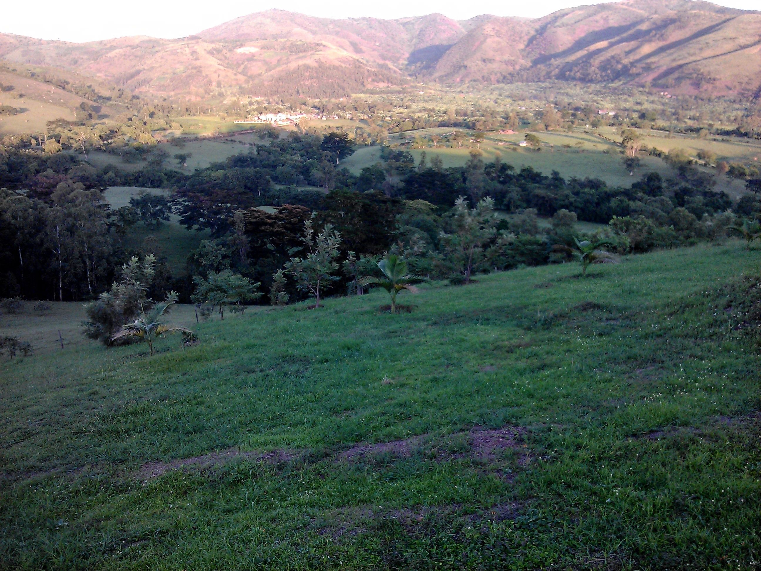Paisaje rural con colinas onduladas, árboles dispersos y un pequeño asentamiento a lo lejos.