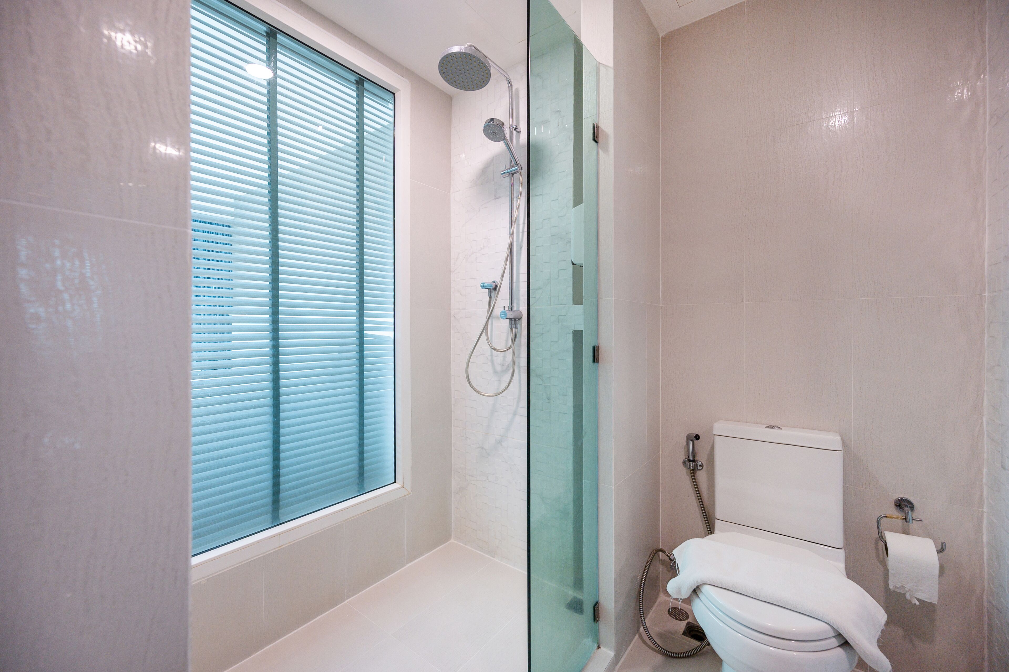 A modern bathroom with a glass-enclosed shower, a toilet, and a window with blinds.