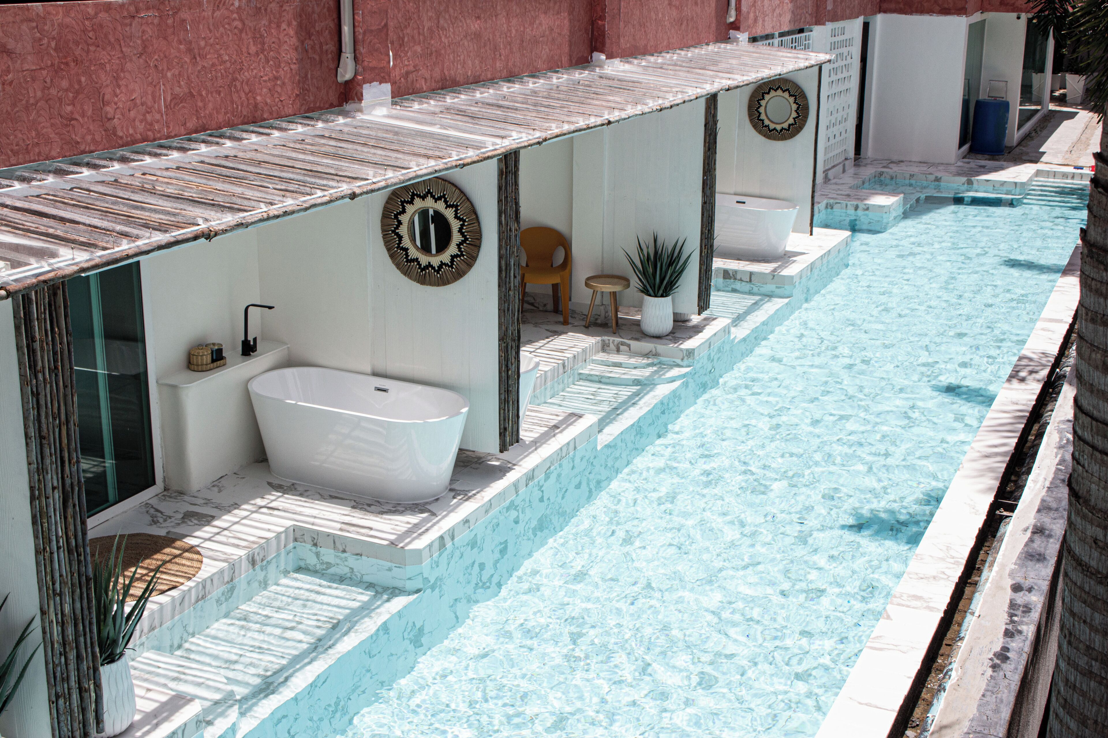A poolside area with a large bathtub, a chair, and a potted plant.