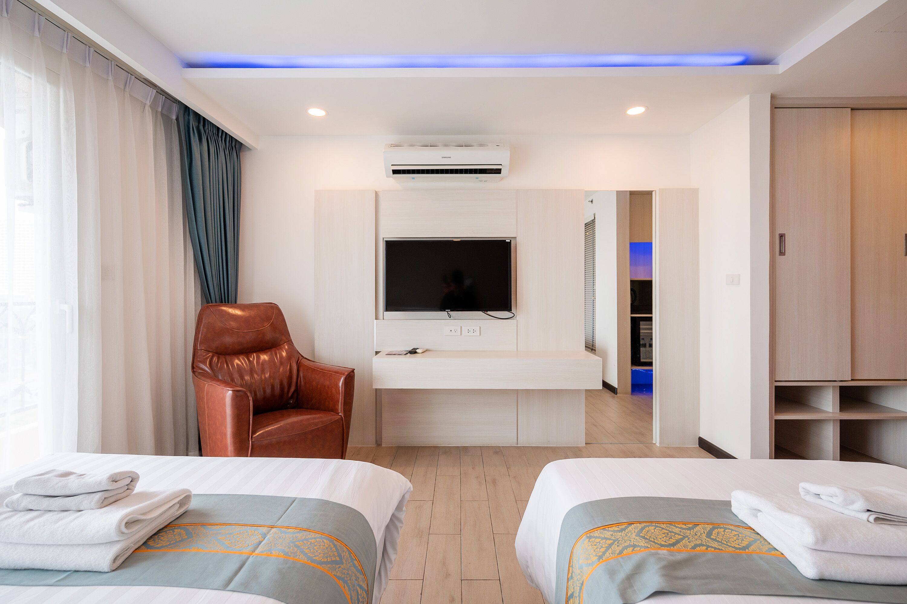 A hotel room with two beds, a desk with a flat-screen TV, a leather chair, and a wardrobe.