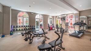 Una palestra con attrezzature per esercizi, ampie finestre e pavimento in legno.