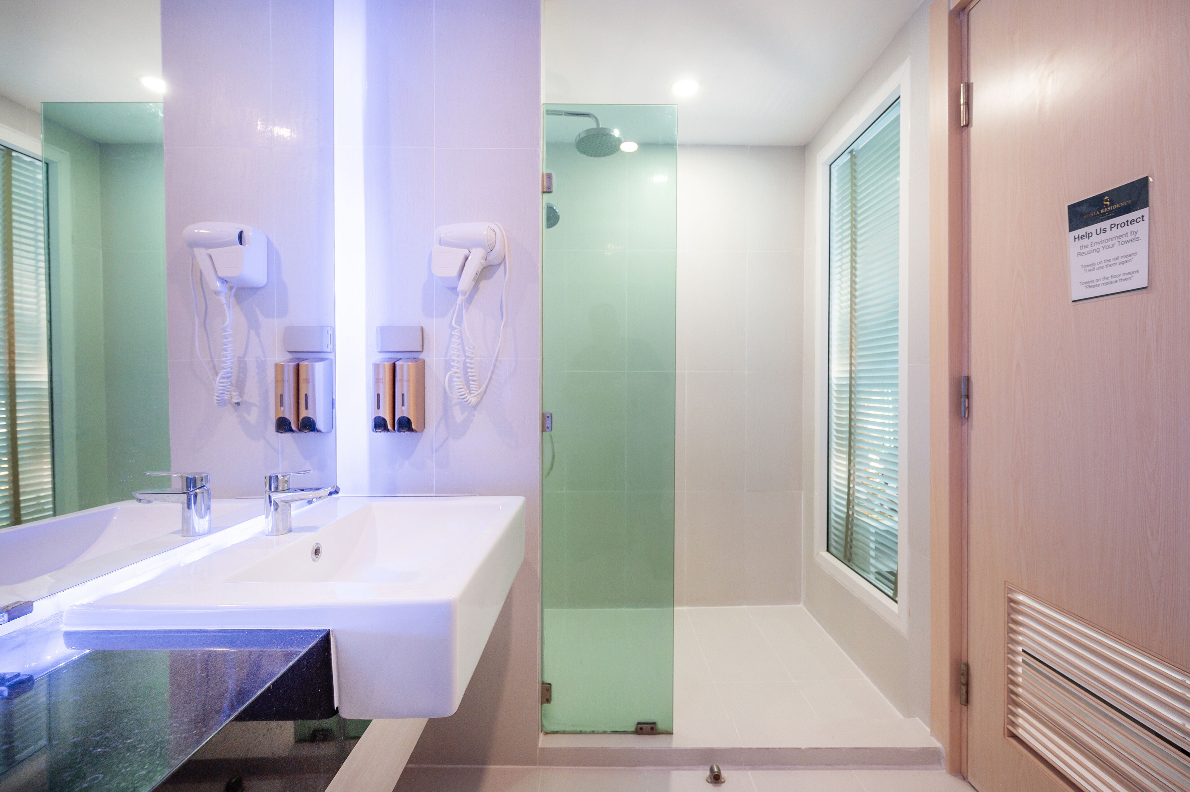A modern bathroom with a large sink, a glass shower enclosure, and a towel dispenser.