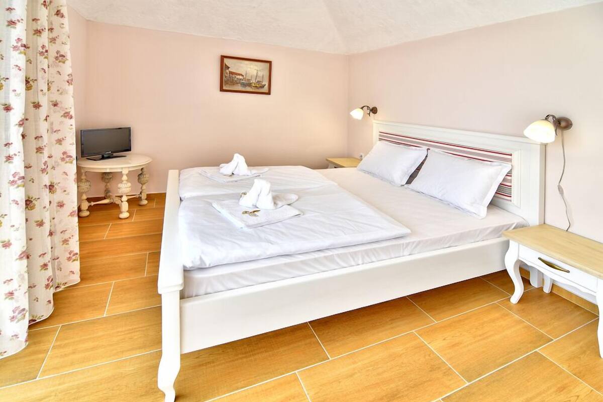 Un lit double avec du linge de lit blanc, une table de chevet, une lampe et un tableau au mur.