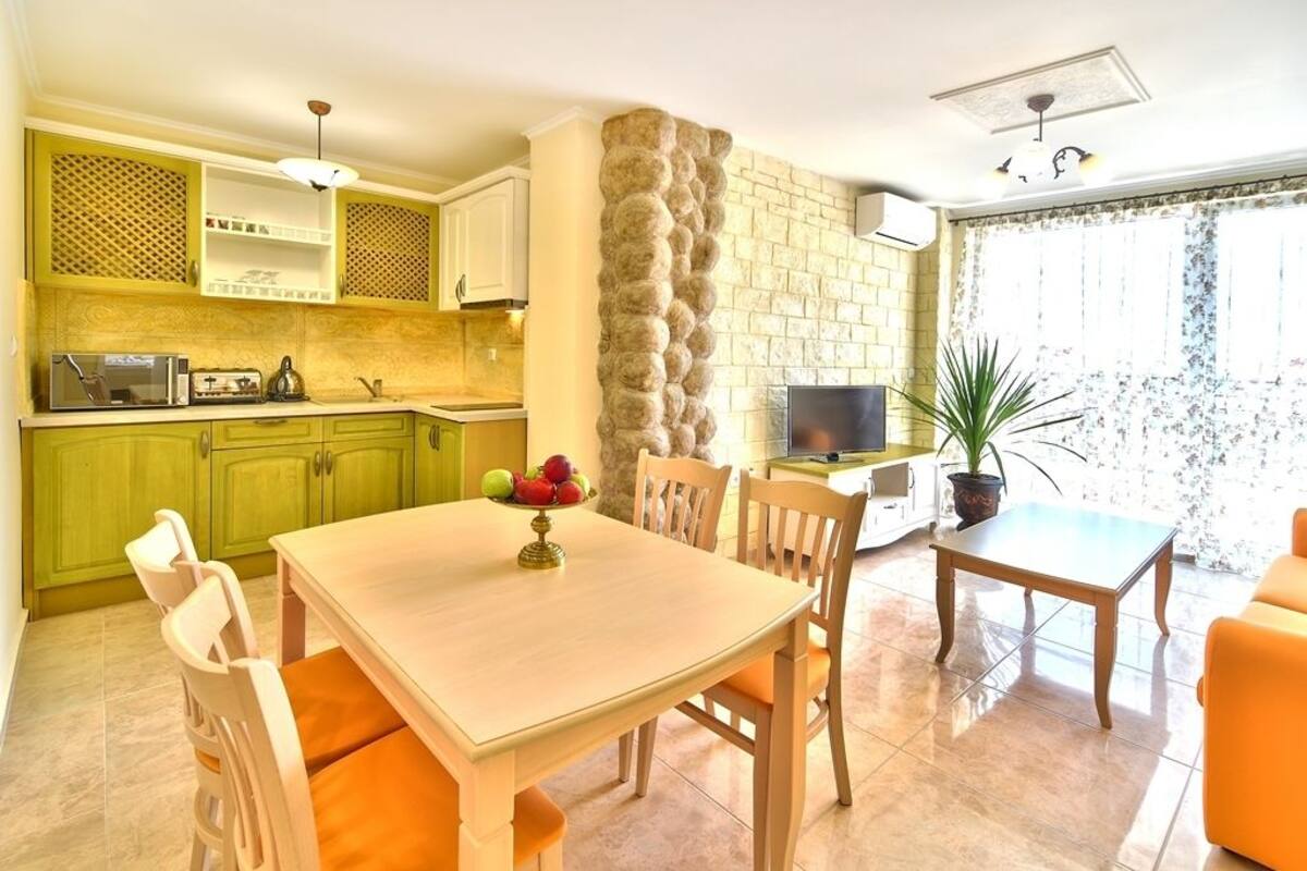 Une cuisine moderne avec des meubles de couleur verte, un mur d’accent en pierre et un coin repas comprenant une table et des chaises.