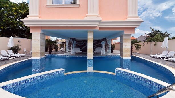 A swimming pool with a tiled edge, surrounded by lounge chairs and a covered seating area. - Family Hotel Sirena Palace (Obzor)