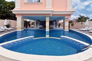 A swimming pool with a tiled edge, surrounded by lounge chairs and a covered seating area.