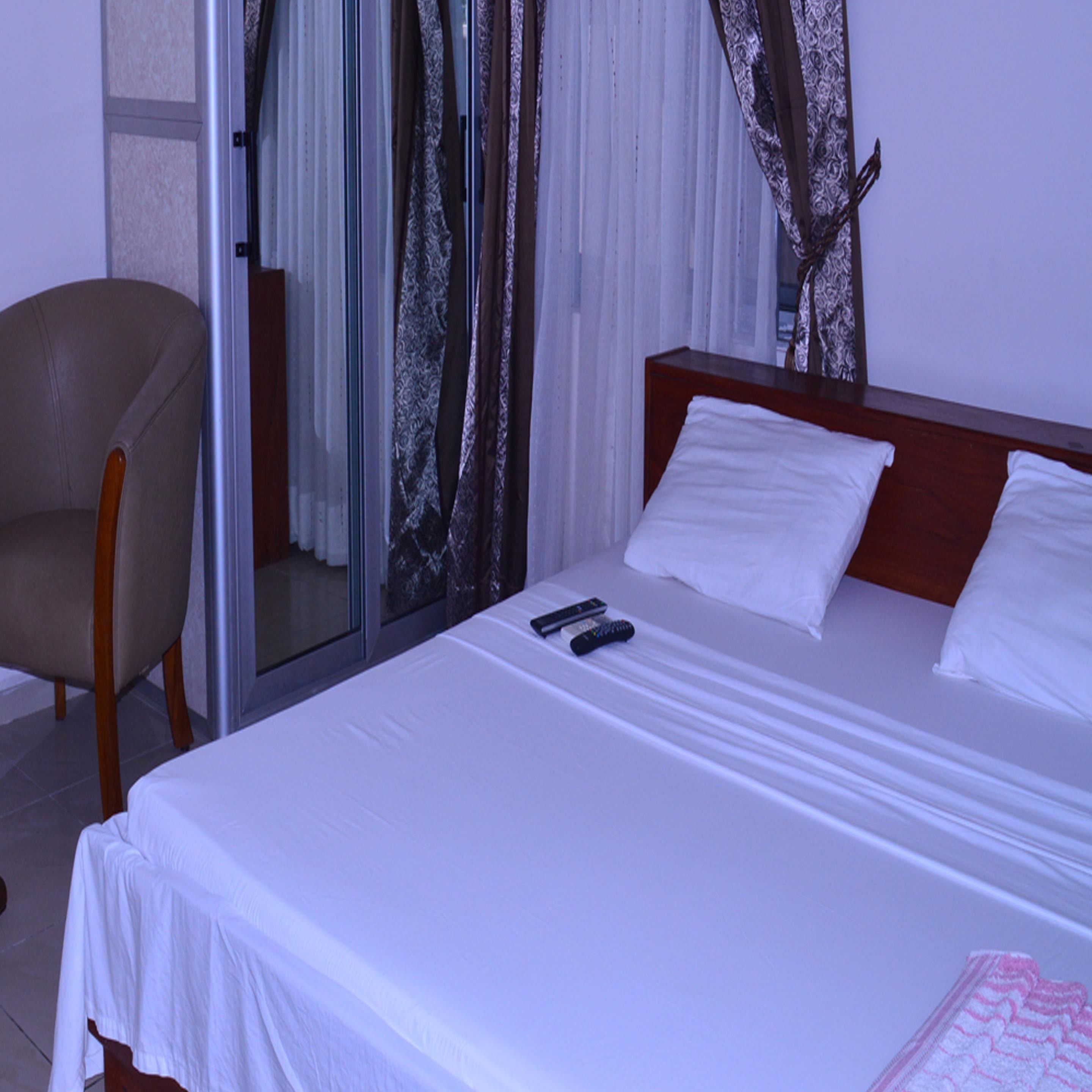 Habitación de hotel con cama, una silla y un ventanal que da a un balcón.