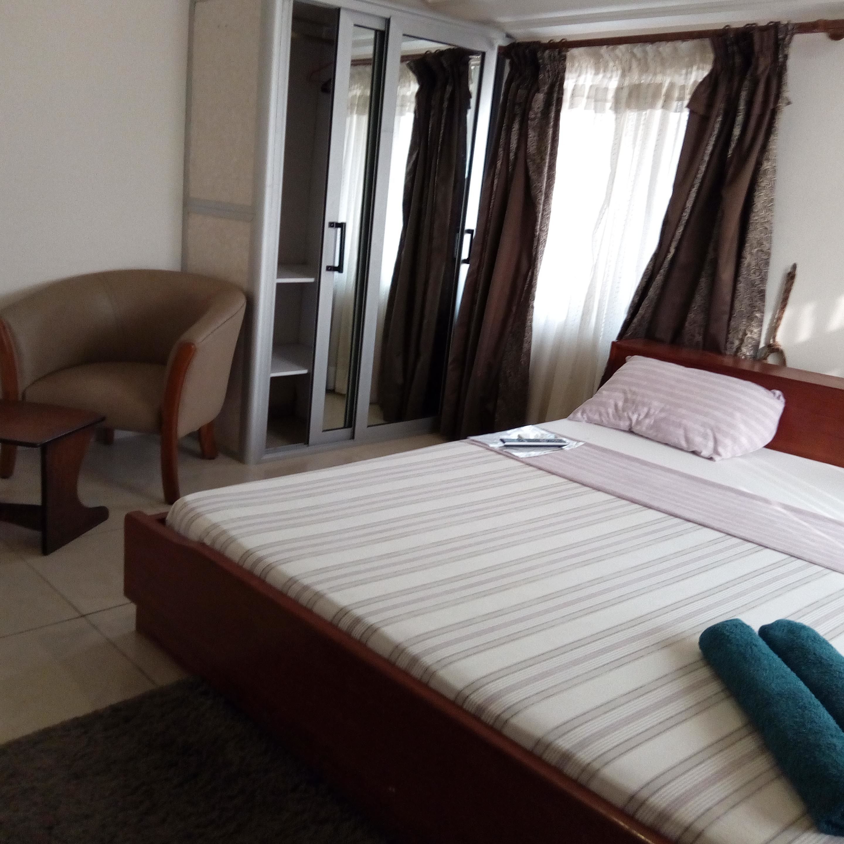Une chambre d’hôtel avec un lit, une chaise, une armoire et des rideaux.