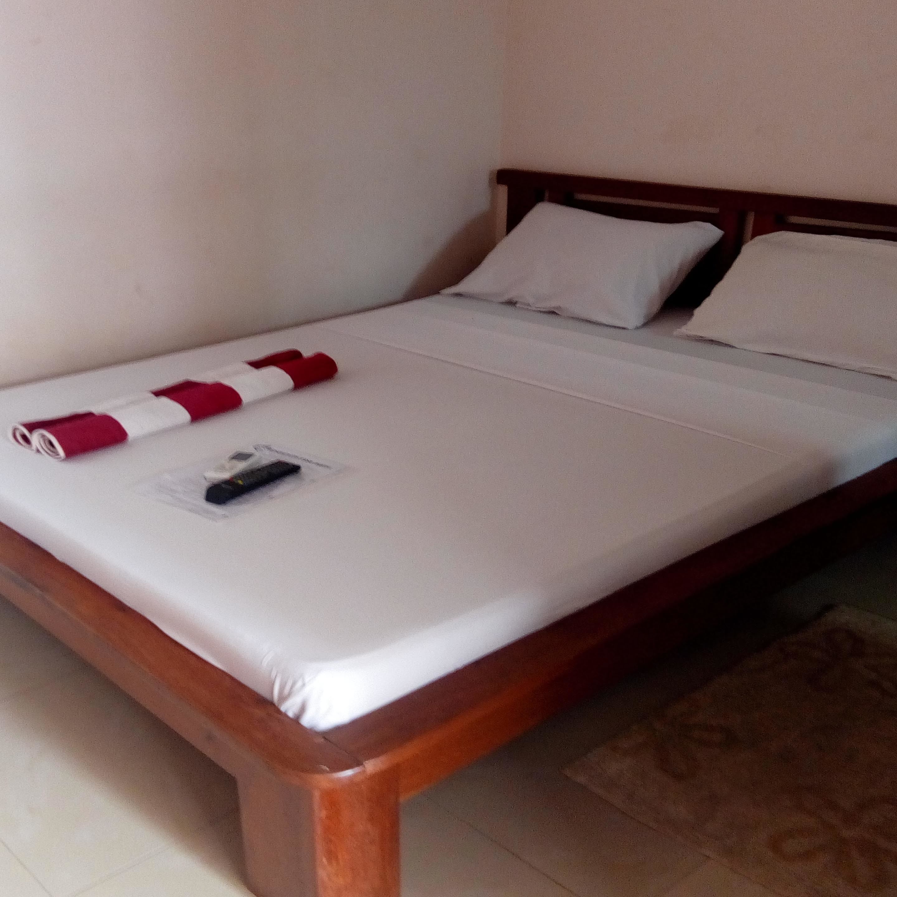 Een opgemaakt bed met een witte matras en een rood-wit gestreepte deken.