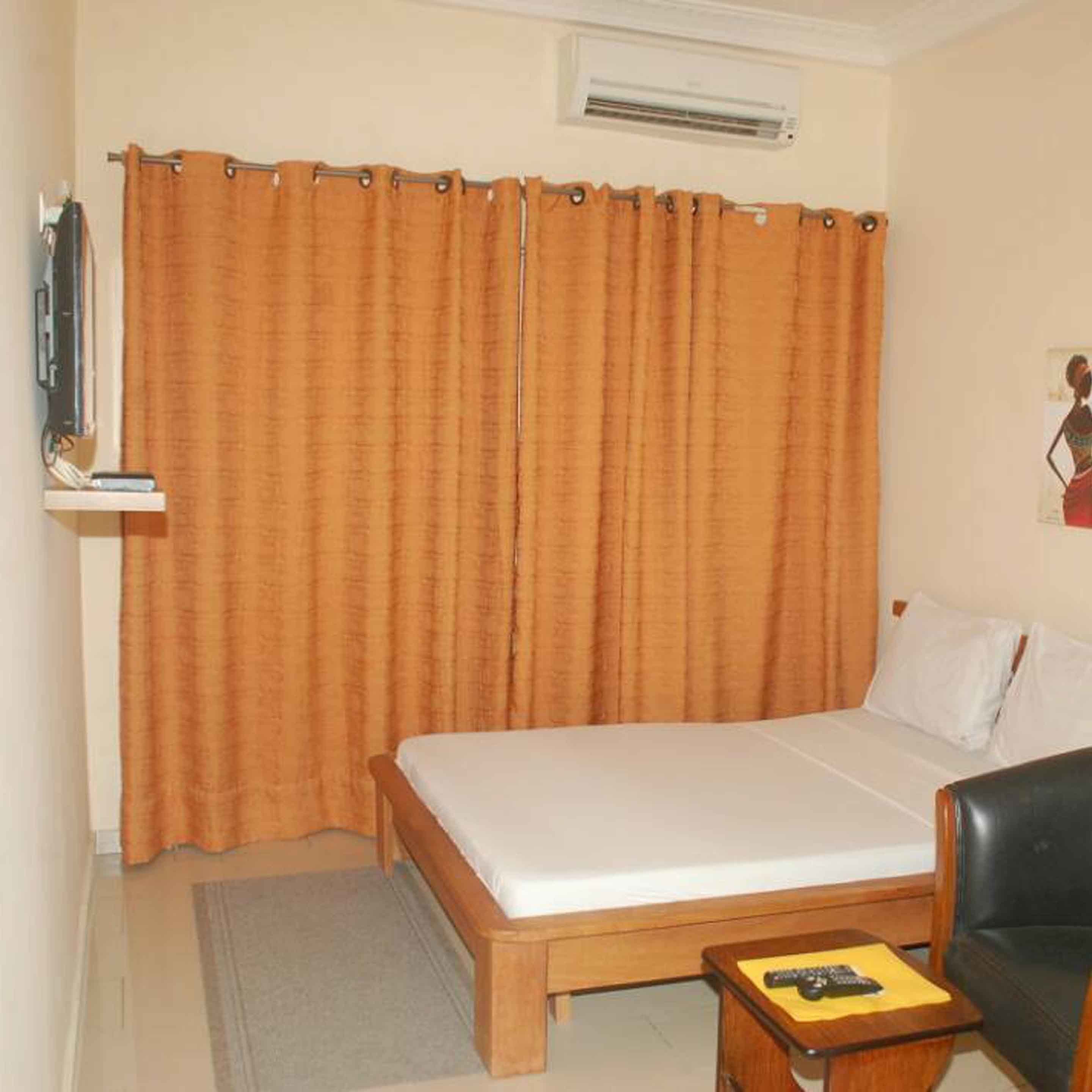 Un dormitorio con cama, una silla, una mesita y una cortina.