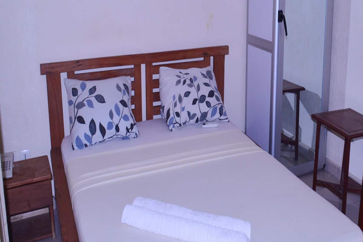 Una cama bien hecha con cabecera de madera, dos almohadas con diseño de hojas y una toalla blanca enrollada.