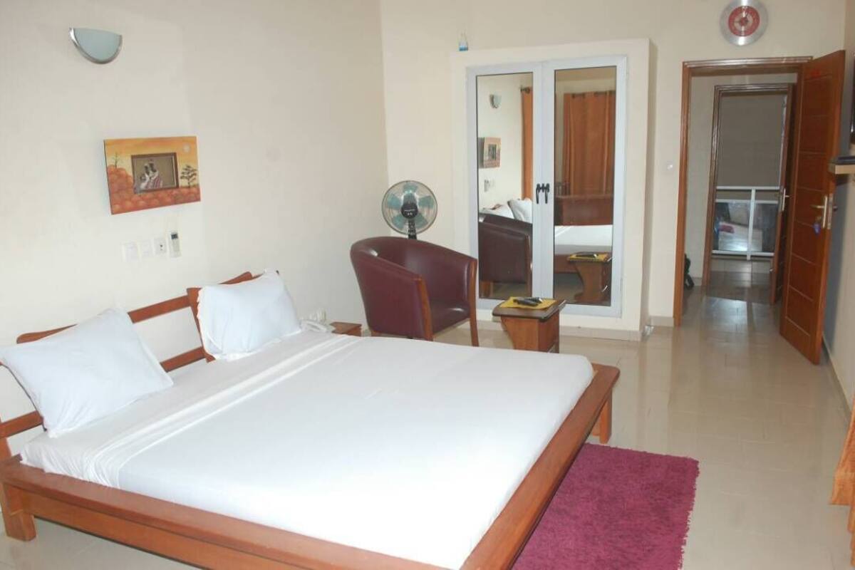 Habitación de hotel con cama, una silla, escritorio, espejo y puerta que da a otra habitación.