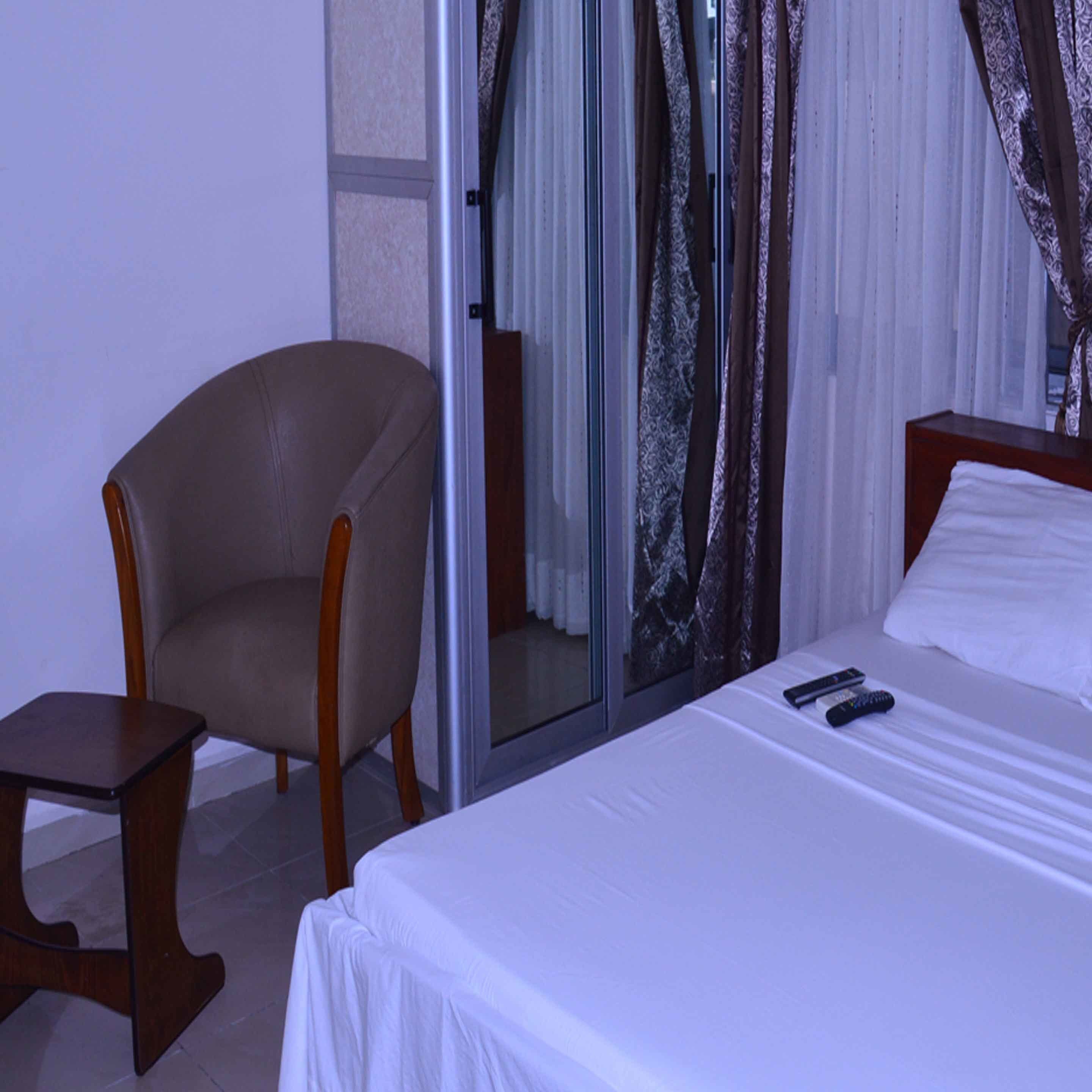A hotel room with a bed, a chair, a small table, and a glass door leading to a bathroom.