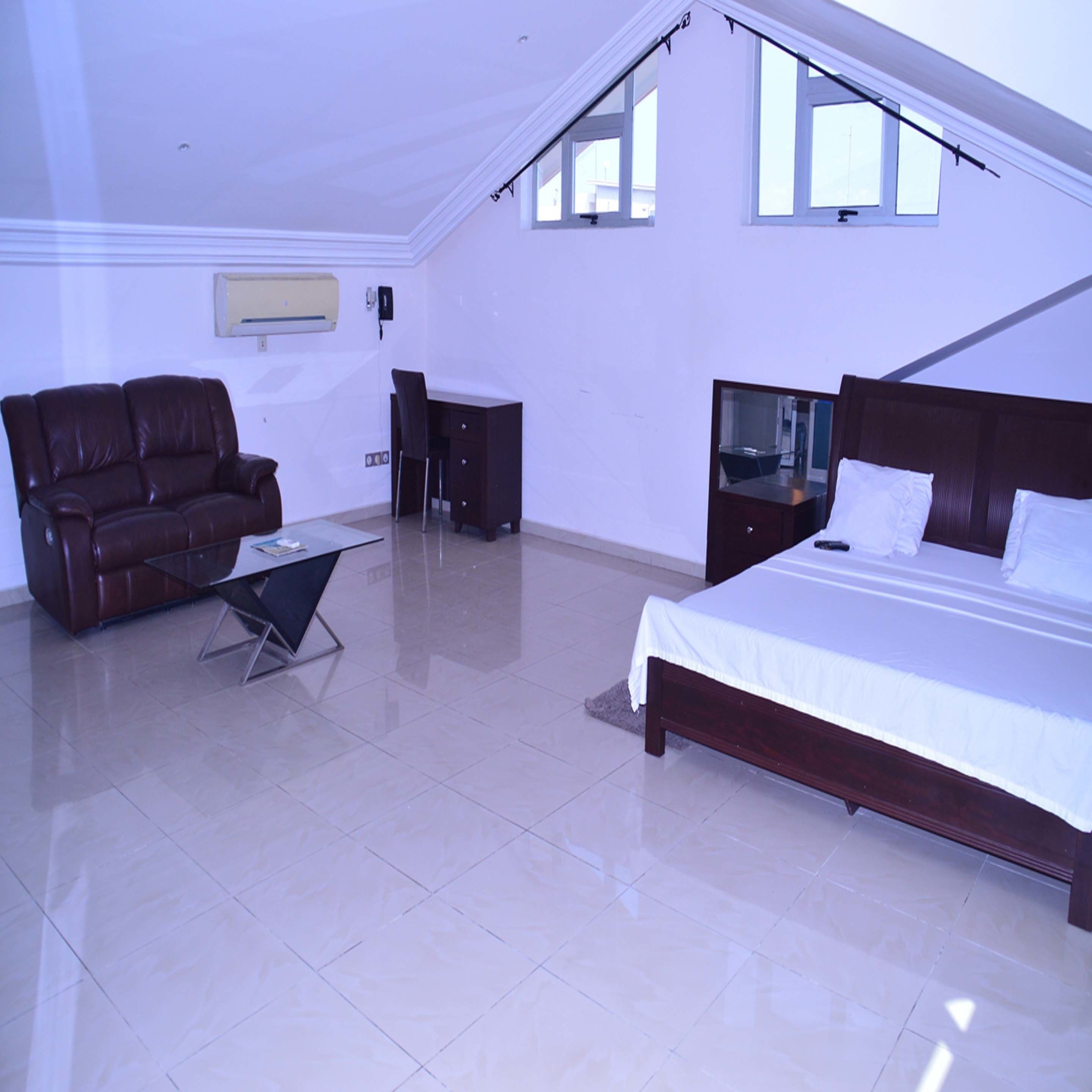 A bedroom with a bed, a desk, a chair, and a sofa.